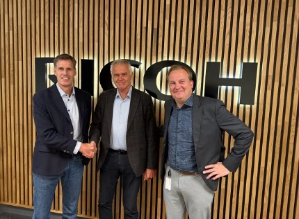Three men standing indoors in front of a wooden slat wal
